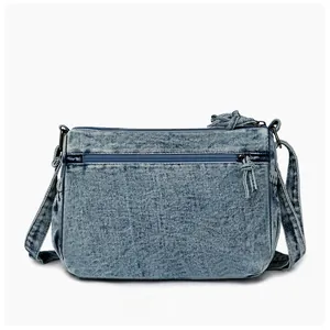 Detail view of the reverse side of blue washed denim crossbody bag with multiple zippers