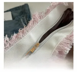 Detailed close-up of a white canvas tote bag with pink tassel trim and golden zipper