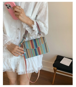 Detail of colorful woven shoulder bag featuring vertical rainbow stripes and soft cord handles