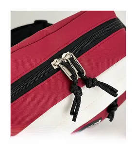 Detail of a red and white canvas messenger bag featuring smooth black double zippers