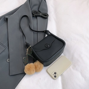 Retro black leather crossbody bag with wave edge lid and cherry tassel charm on grey suit