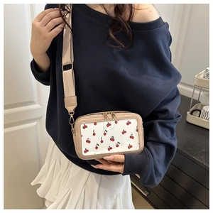 Detail of white crossbody bag with cherry prints and wide nylon shoulder strap
