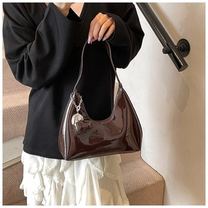 Detail of glossy chocolate brown patent leather shoulder bag with heart charm accessory