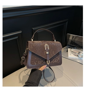 Detail of dark brown faux leather bag with snake texture and gold U-shaped lock buckle