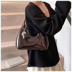 Detail of dark brown patent leather baguette bag with heart charm and silver chain