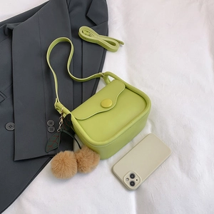 Minimalist avocado green crossbody bag with plush charm on stylish blazer background