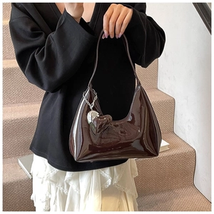 Detail of dark brown patent leather baguette bag with a heart-shaped charm and glossy finish
