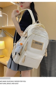 Detail view of cream nylon backpack with leather accents and a cute duckling pendant