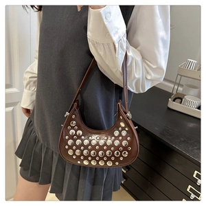 Detail of coffee brown leather crescent bag featuring silver studs on a shoulder strap