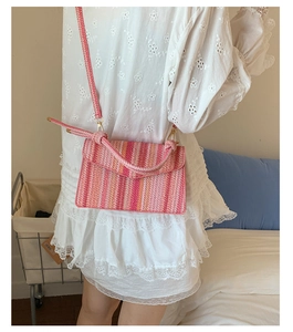 Detail view of a colorful striped woven straw crossbody bag with metal buckle closure
