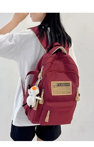 Detail of burgundy nylon backpack with side buckles, fashion label, and white duck charm