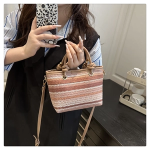 Détail du sac en paille tissé avec rayures dégradées et poignée en cuir marron nouée