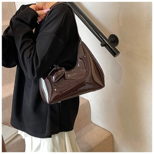 Brown patent leather hobo bag with heart charm shown on model in modern indoor setting