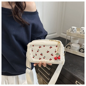 Detail of white cherry print square crossbody bag with wide strap and cherry charm