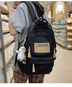 Detail of black high-capacity backpack with leather label and white duck pendant