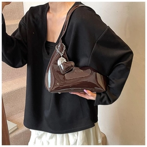 Detail of dark brown patent leather armpit bag with glossy finish and silver heart charm