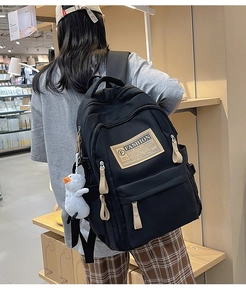 Detail of black large capacity school backpack with fashion patch and plush duck charm