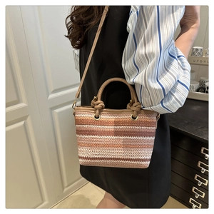 Détail d'un sac seau en paille tissée à rayures colorées et poignée en similicuir