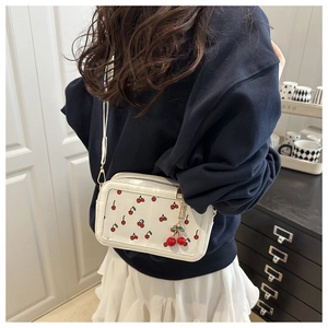 Detailed shot of white cherry print crossbody bag with cute 3D cherry charm and strap