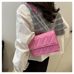 Détail du sac à bandoulière rose fuchsia avec gaufrage géométrique porté par un mannequin