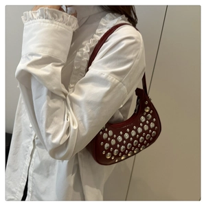 Detail view of burgundy crescent bag featuring decorative silver metal rivets and leather texture