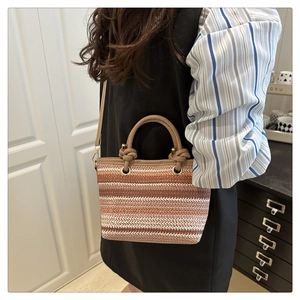 Détail d'un sac seau tissé rayé avec poignée en cuir porté par un mannequin