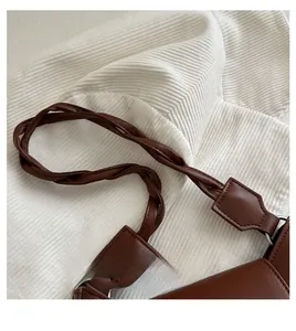 Dettaglio di una borsa in pelle marrone con manico intrecciato e anelli metallici di collegamento