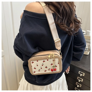 Detailed view of cream crossbody bag with red cherry prints and wide fabric shoulder strap