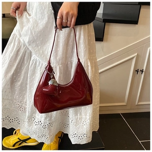 Detail of dark red patent leather baguette bag with silver chain and heart charm