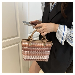 Détail du sac seau en paille tressée avec rayures dégradées et poignée en cuir nouée