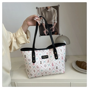 Detail of white tote bag with cute cartoon prints and black shoulder strap held by hand