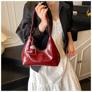 Close-up of glossy wine red patent leather shoulder bag with silver heart charm detail