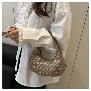 Detail view of a taupe crescent bag with silver rivets worn by a model for size