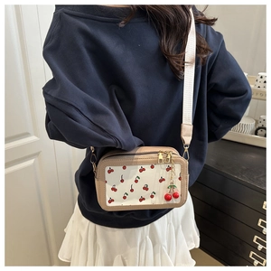 Close-up of beige square crossbody bag with red cherry prints and wide fabric strap
