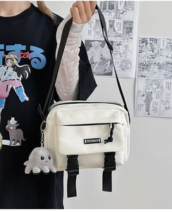 Close-up of white canvas utility crossbody bag with black buckles and octopus plush pendant