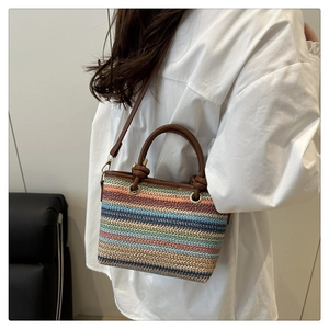 Détail d'un sac seau en paille tissée multicolore avec poignées en cuir brun et nœuds