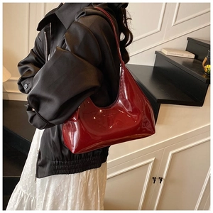 Close-up of a burgundy patent leather hobo bag worn by a model in a minimalist indoor setting