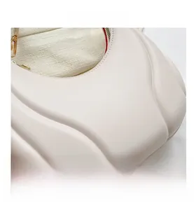 Detail of white textured shoulder bag with gold hardware and vibrant red interior lining