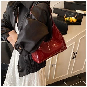 Detail of dark red glossy patent leather baguette bag worn over the shoulder