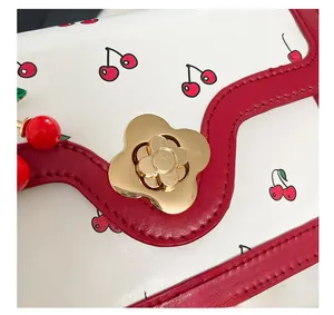 Detail view of cream handbag featuring cherry print and golden flower shaped twist lock