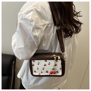 Close-up of small square crossbody bag featuring cherry print and wide shoulder strap