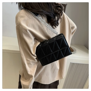 Détail d'un sac bandoulière matelassé noir avec chaîne argentée sur un modèle