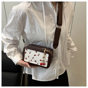 Detail of crossbody bag featuring cherry print, wide strap and cute cherry charm