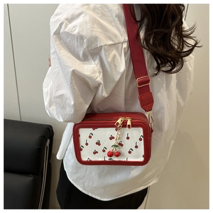 Detail of red cherry print crossbody bag with wide strap and cherry metal zipper charm