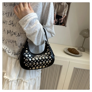 Detail of black crescent hobo bag with silver studs worn by model in cozy home setting