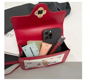 Detail showing inner capacity of cherry print crossbody bag with items and metal lock