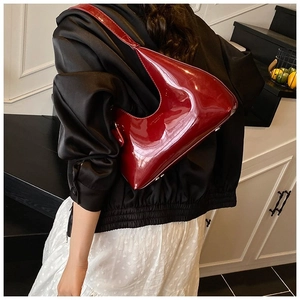 Detail shot of the asymmetrical dark red patent leather baguette bag worn over the shoulder