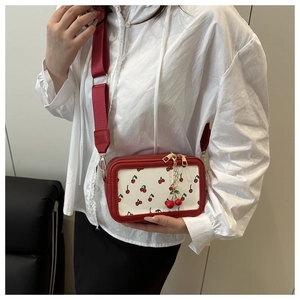 Fashionable crossbody camera bag with cherry print, wide red strap, and cherry charm detail