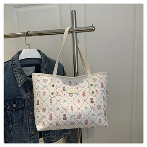 Close-up of white tote bag with cartoon prints and gold brand name plaque on the front