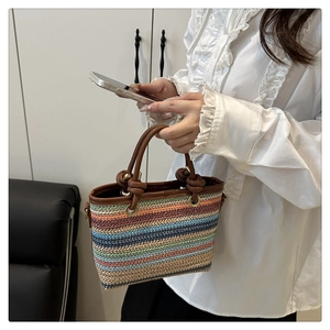 Détail d'un sac seau en paille colorée avec poignées nouées en cuir marron et anneaux